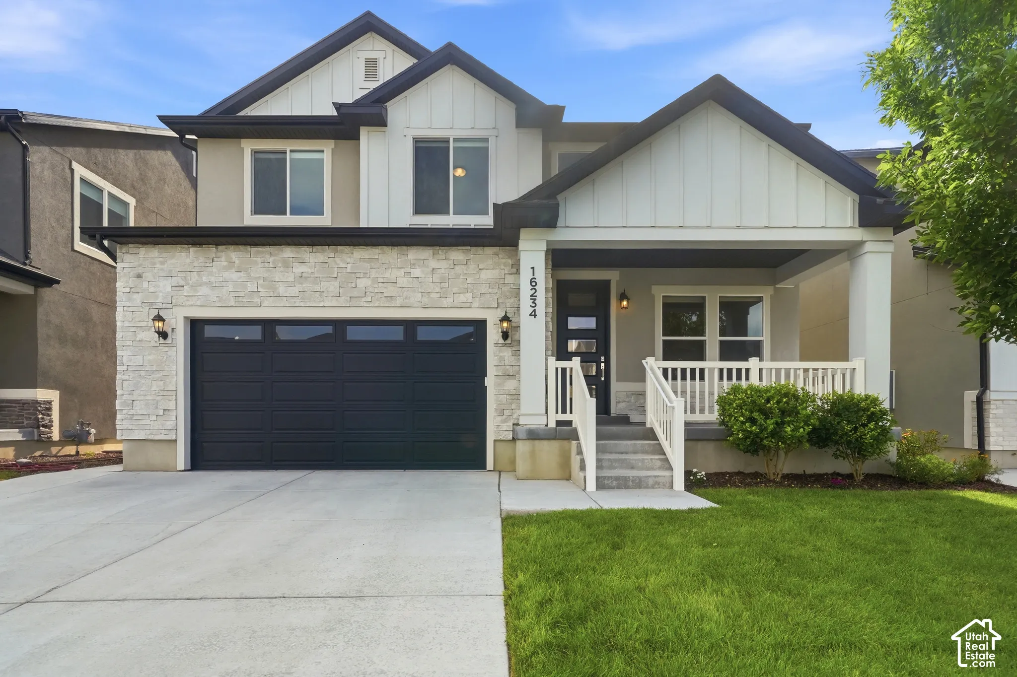 Modern facade featuring a stone veneer accent, attached two-car garage with a dark door, and a covered front porch with white railings