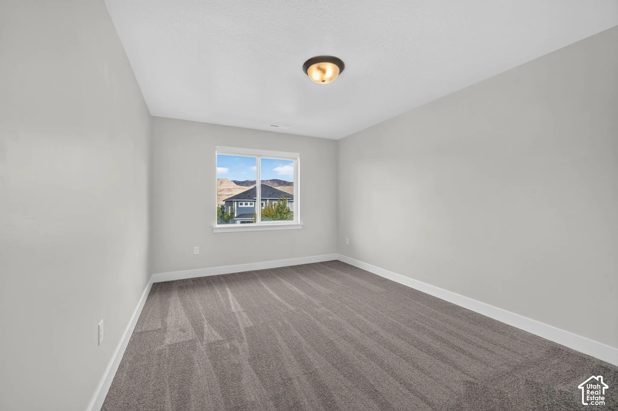 Bright, freshly finished bedroom showcasing neutral wall finishes, wood-finish flooring with linear striping detail, and abundant natural light from a large window framing scenic mountain and residential backdrop