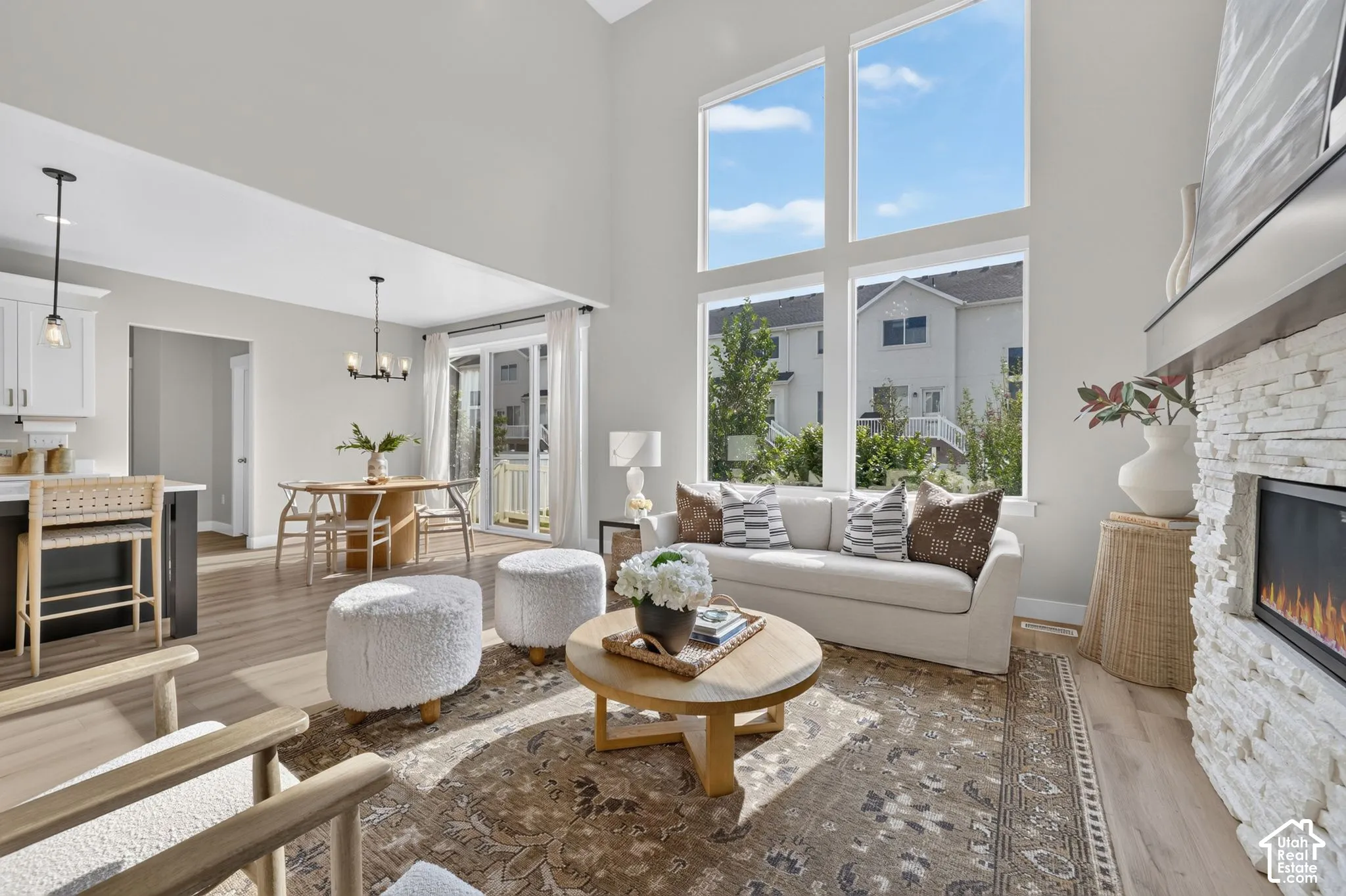 Vaulted ceiling living area featuring large picture windows, a stone-faced fireplace, wood-finish flooring, and an open concept layout with an adjacent dining space