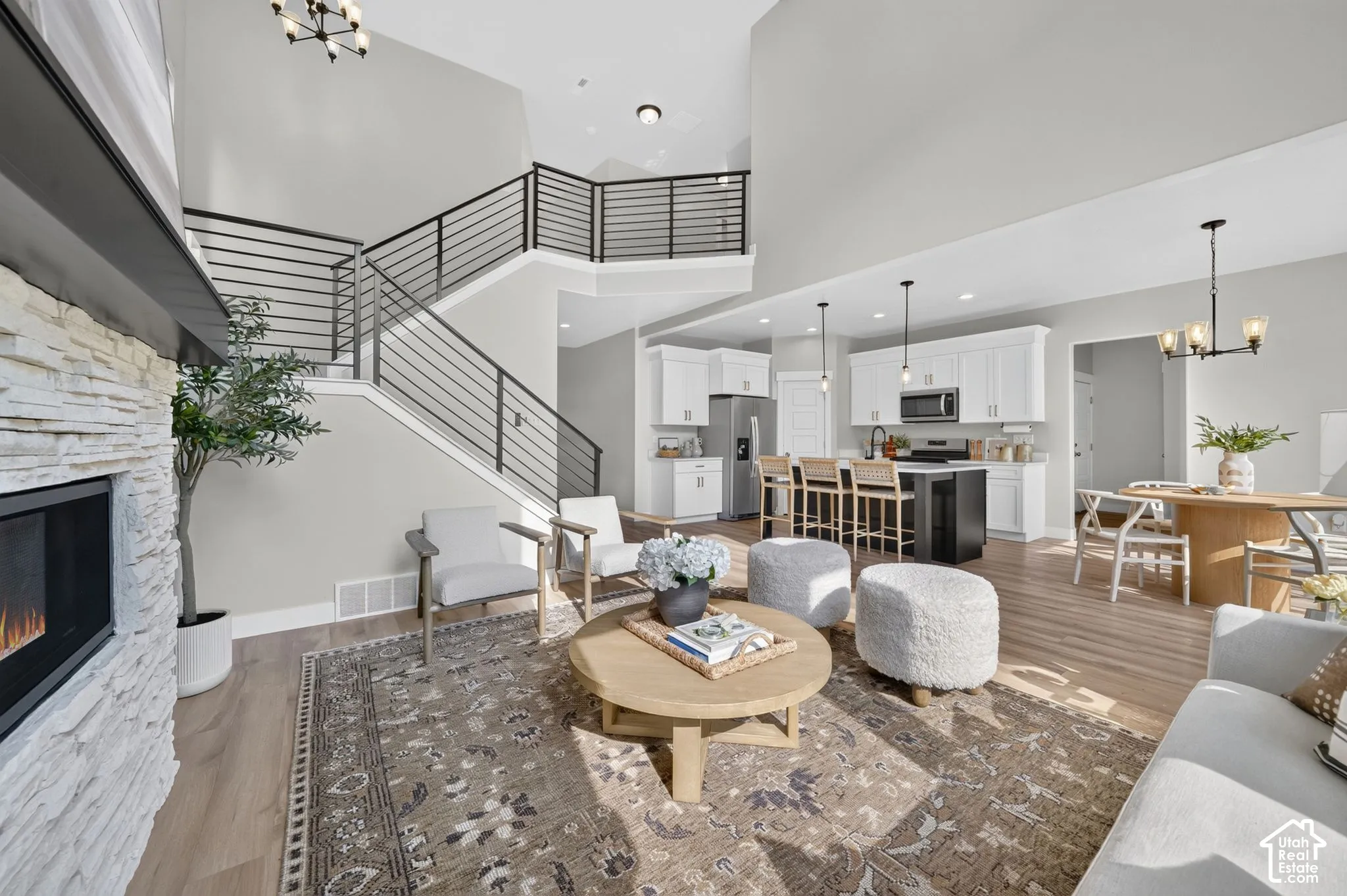 Open-concept living area featuring a wood-finish plank floor, gas fireplace with white brick surround, curved staircase with horizontal metal railings, and abundant natural light from skylights