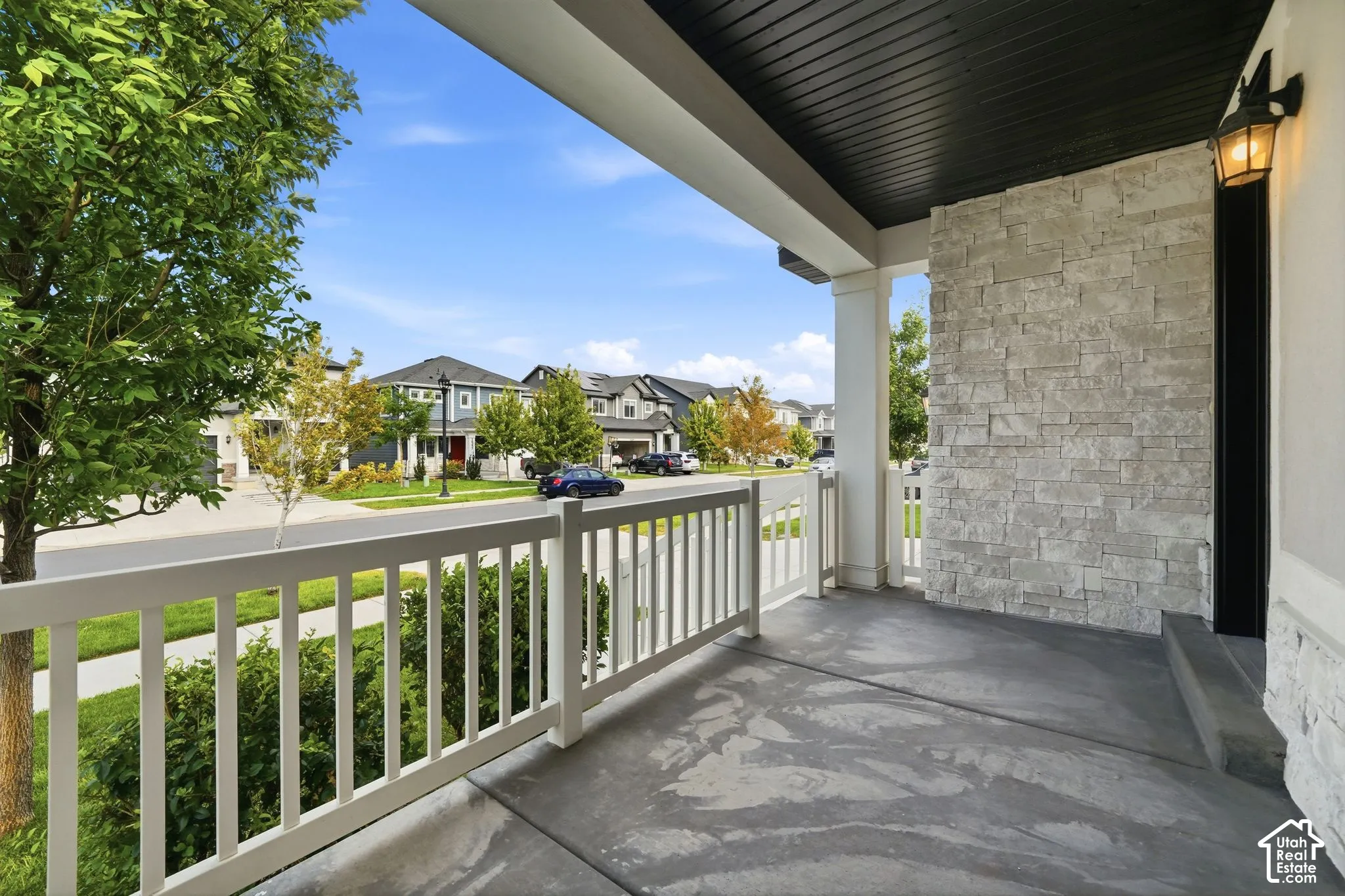 Covered front porch with a concrete surface, white railing, decorative stone accent wall, and an attached exterior light fixture