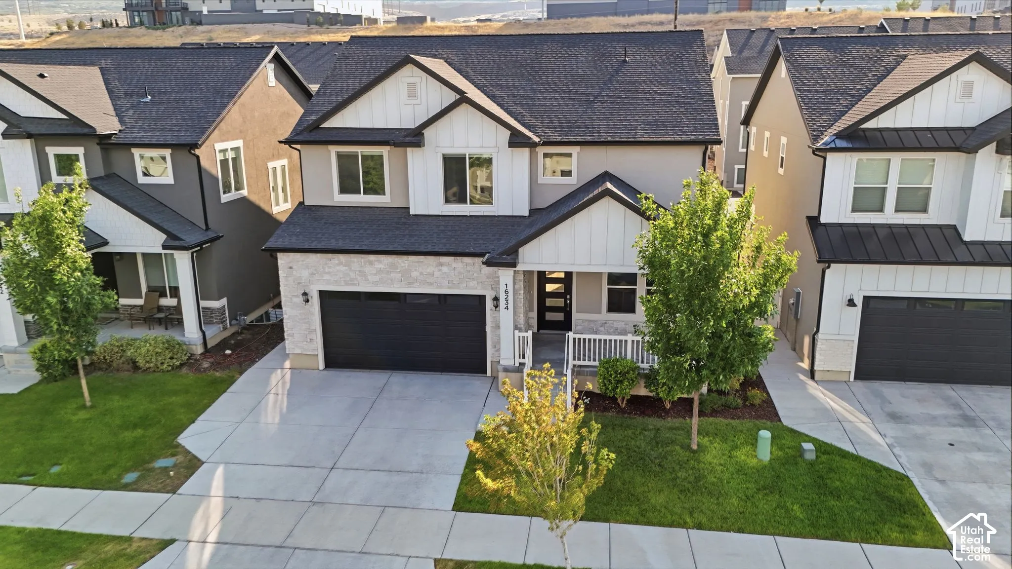 Modern two-story residence featuring a two-car garage, white railing porch, and a black shingle roof