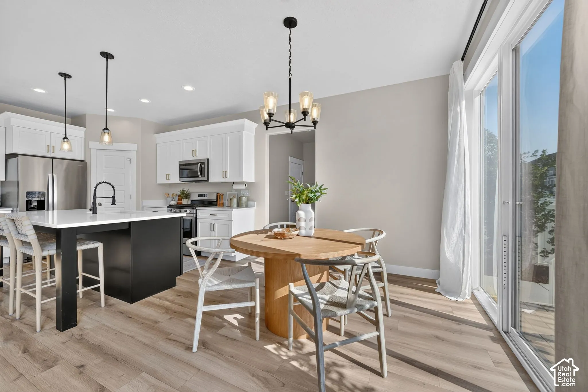 Kitchen and dining area featuring a kitchen island with white countertop, white cabinetry with stainless steel appliances, wood-finish flooring, and sliding glass doors