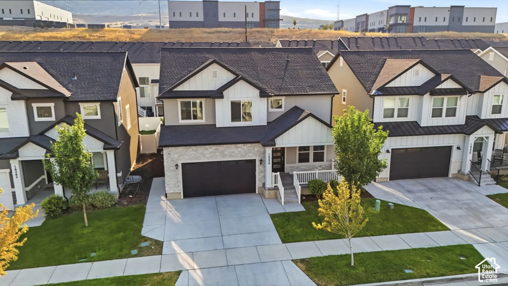 Two-story residence featuring a dark asphalt shingle roof, light-colored stone and vertical panel siding, dark garage door, and a concrete driveway