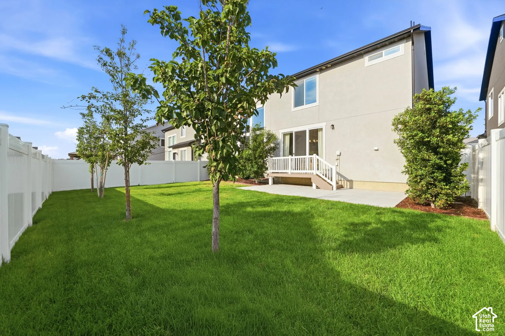 Expansive backyard with a manicured lawn, established trees, privacy fencing, a concrete patio, and a deck with white railings