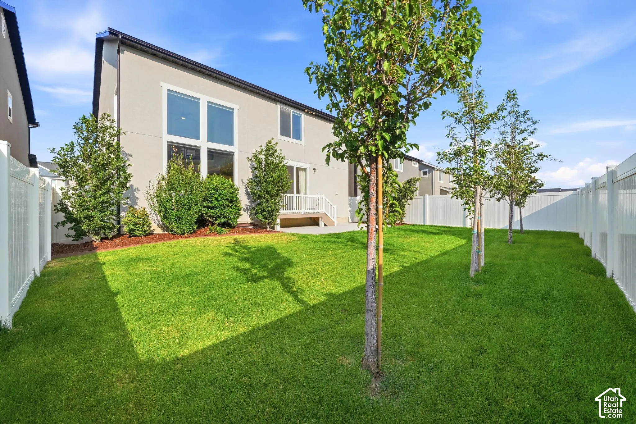 Expansive green lawn with mature trees, a white privacy fence, and a rear deck with white railing