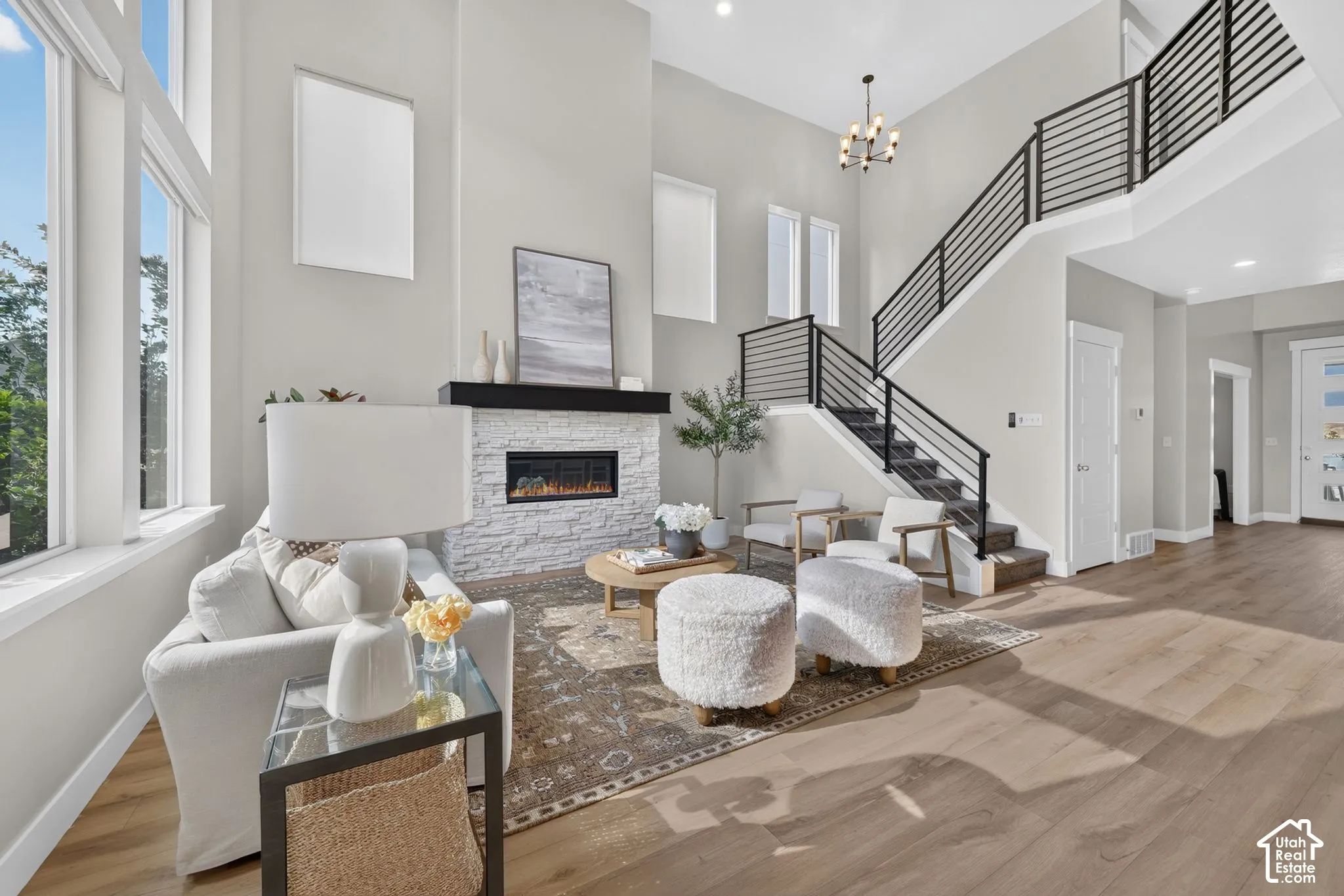 Two-story living area with wood-finish flooring, a contemporary fireplace featuring a white stacked stone surround and dark mantel, and a two-story window array