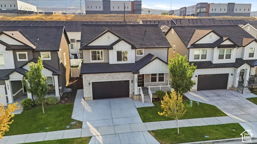 Two-story residence featuring a dark asphalt shingle roof, light-colored stone and vertical panel siding, dark garage door, and a concrete driveway