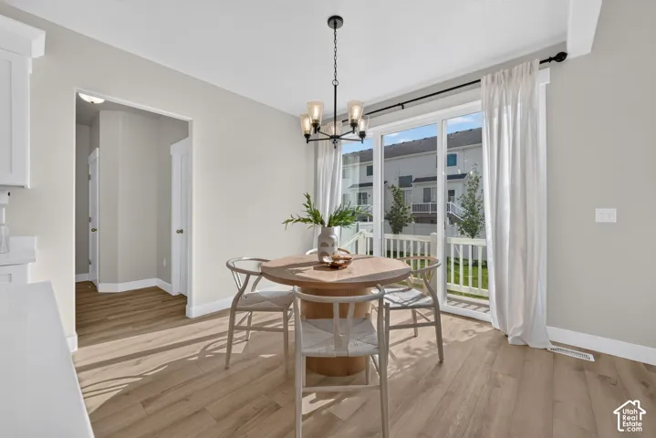 Sliding glass door to outdoor space, overhead chandelier with glass shades, wood-finish flooring, white baseboards, and light neutral wall finishes