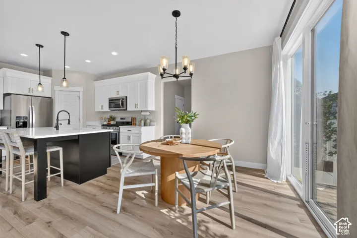 Kitchen and dining area featuring a kitchen island with white countertop, white cabinetry with stainless steel appliances, wood-finish flooring, and sliding glass doors