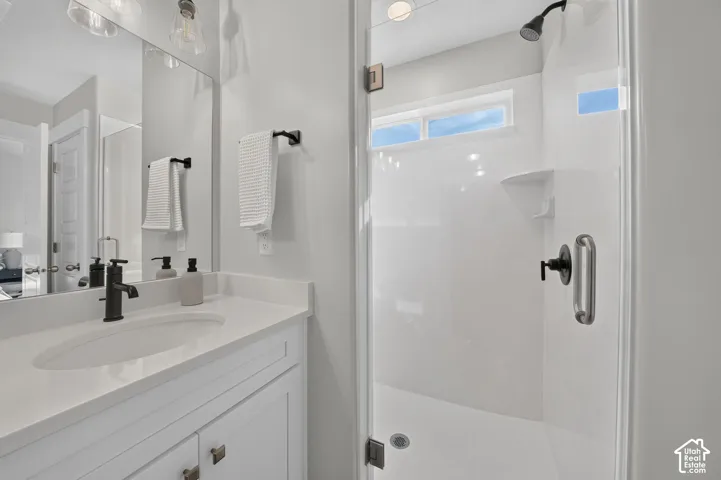 Vanity with a single undermount sink and dark bronze faucet, framed mirror, and glass-enclosed shower with a dark bronze showerhead and a horizontal window