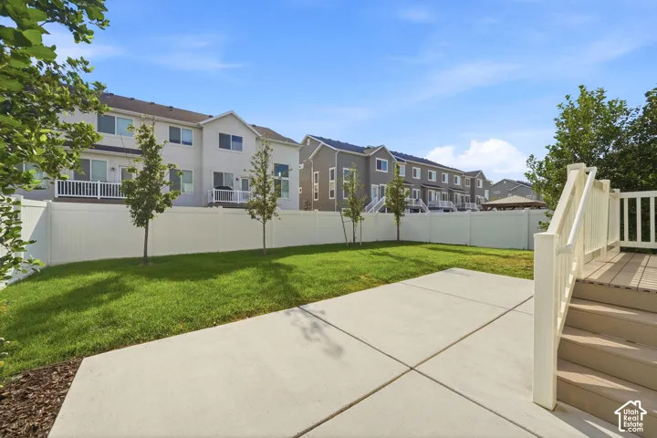 Expansive lawn area with a concrete patio, composite wood decking, and a white privacy fence