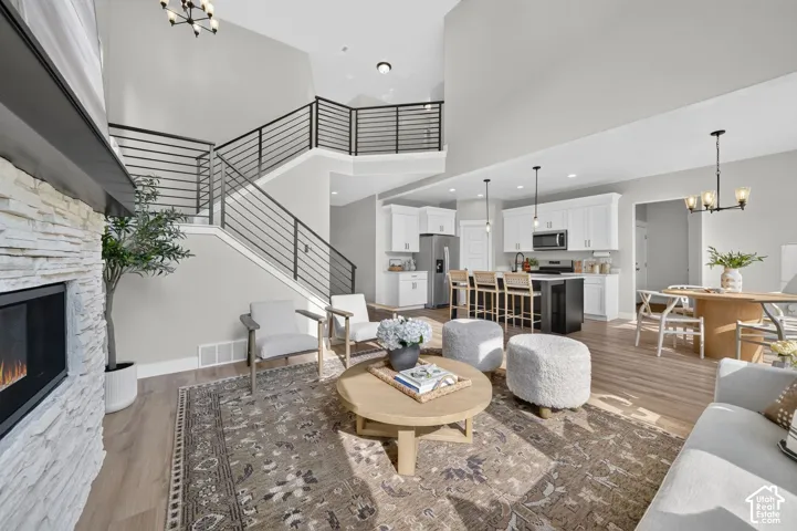 Open-concept living area featuring a wood-finish plank floor, gas fireplace with white brick surround, curved staircase with horizontal metal railings, and abundant natural light from skylights