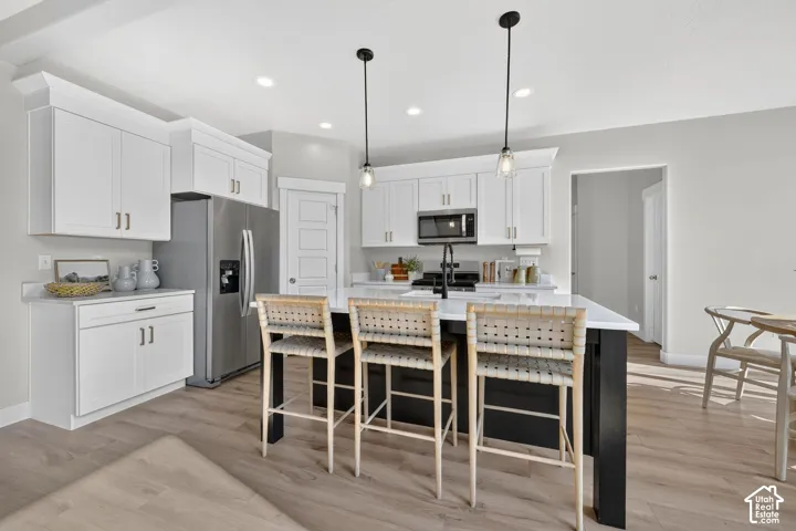 Kitchen featuring white shaker cabinetry, stainless steel refrigerator, built-in microwave, a dark kitchen island, and wood-finish flooring