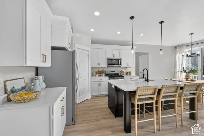 Bright kitchen featuring white cabinetry, a dark-toned island with a light-toned countertop, stainless steel appliances, and wood-finish flooring