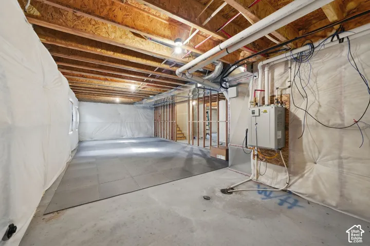 Unfinished lower level featuring exposed wood joist ceilings, concrete flooring, insulated foundation walls, and a wall-mounted tankless water heater