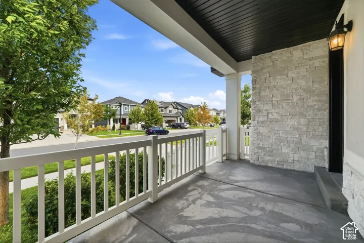 Covered front porch with a concrete surface, white railing, decorative stone accent wall, and an attached exterior light fixture