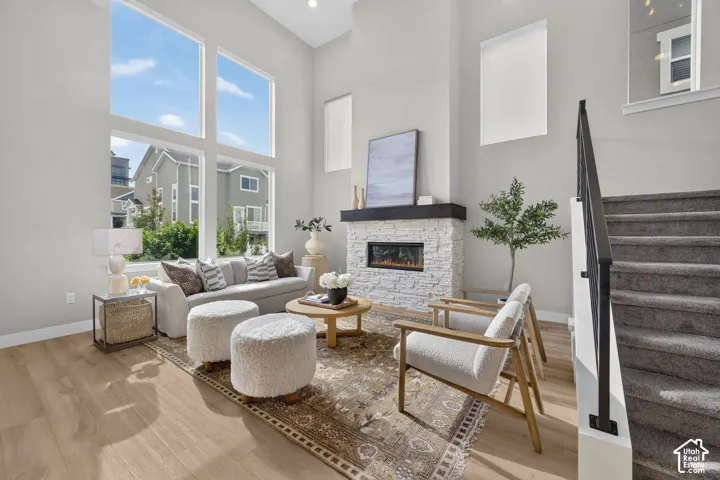 Expansive window wall with multiple panes, stone-clad fireplace with mantel, light wood-finish flooring, and carpeted staircase with black metal railing