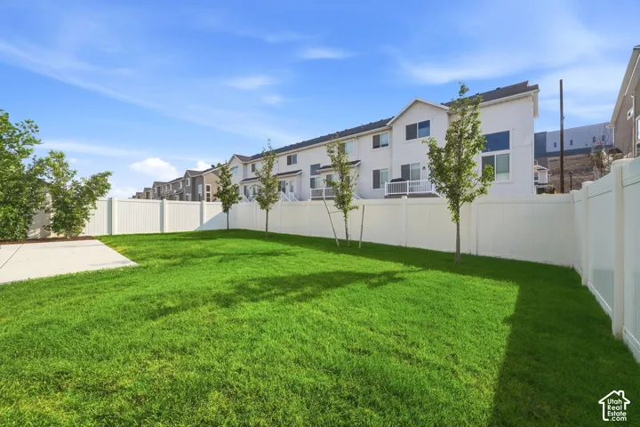 Expansive lawn area with a concrete patio, perimeter fencing, and young trees