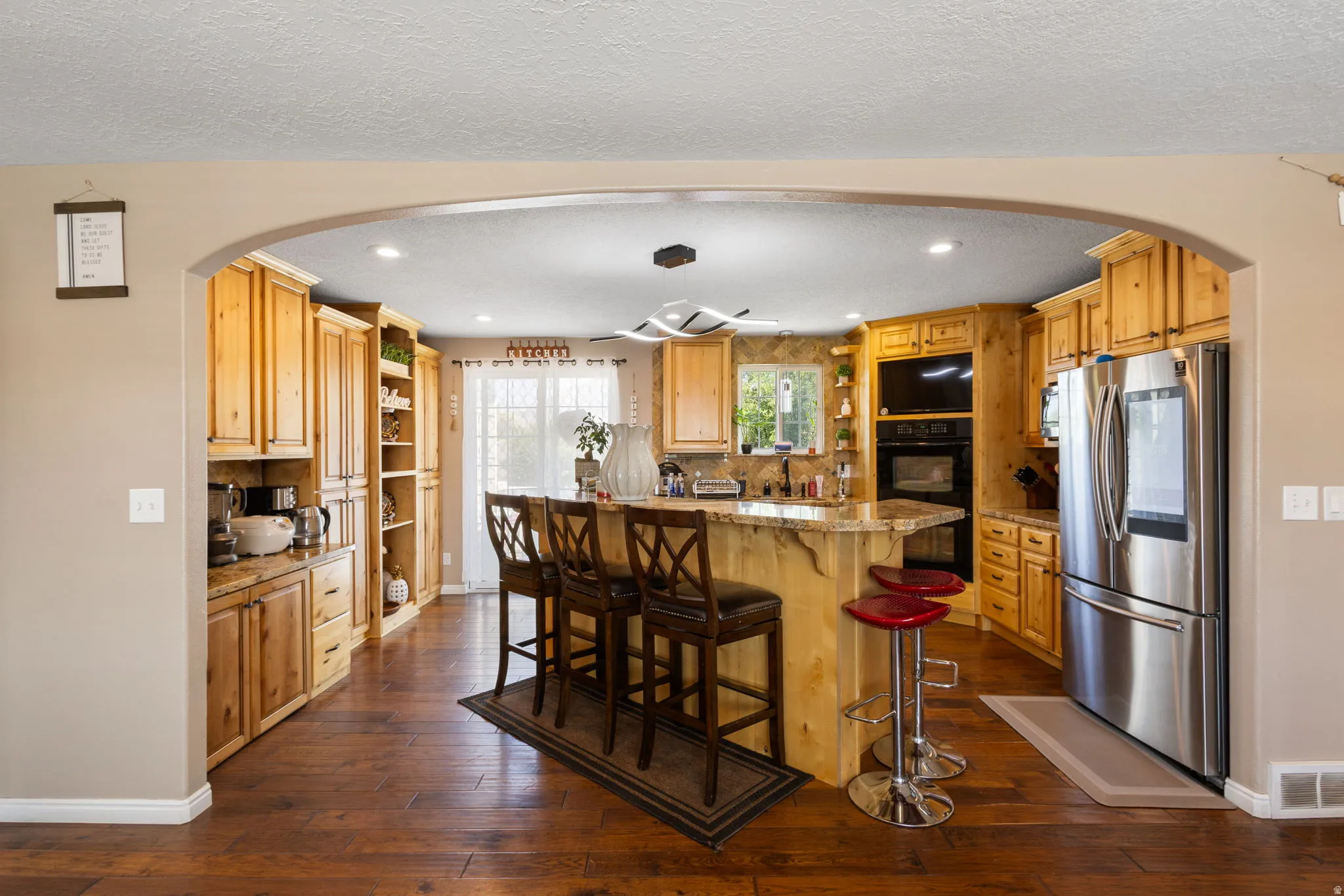 Kitchen featuring a large central island, stainless steel refrigerator, built-in oven, extensive wood cabinetry, and wood-finish flooring