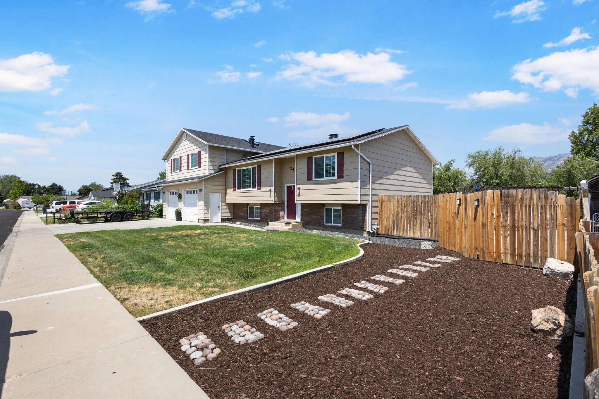 Split-level residence featuring a two-car garage, front yard with green space, and a mulched side yard with a stone paver path