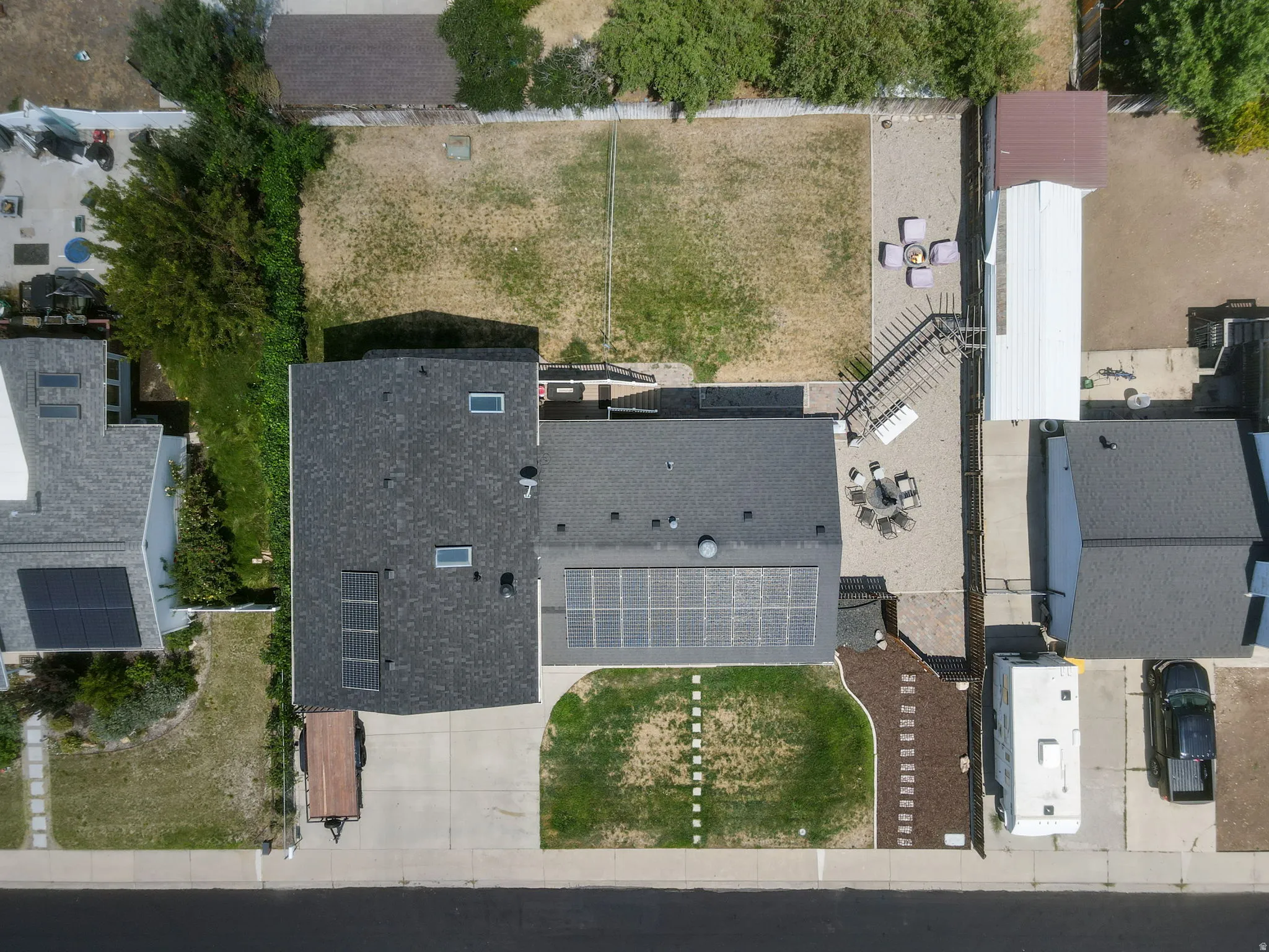 Asphalt shingle roofing, solar panels, concrete driveway, gravel landscaping, and a fenced backyard