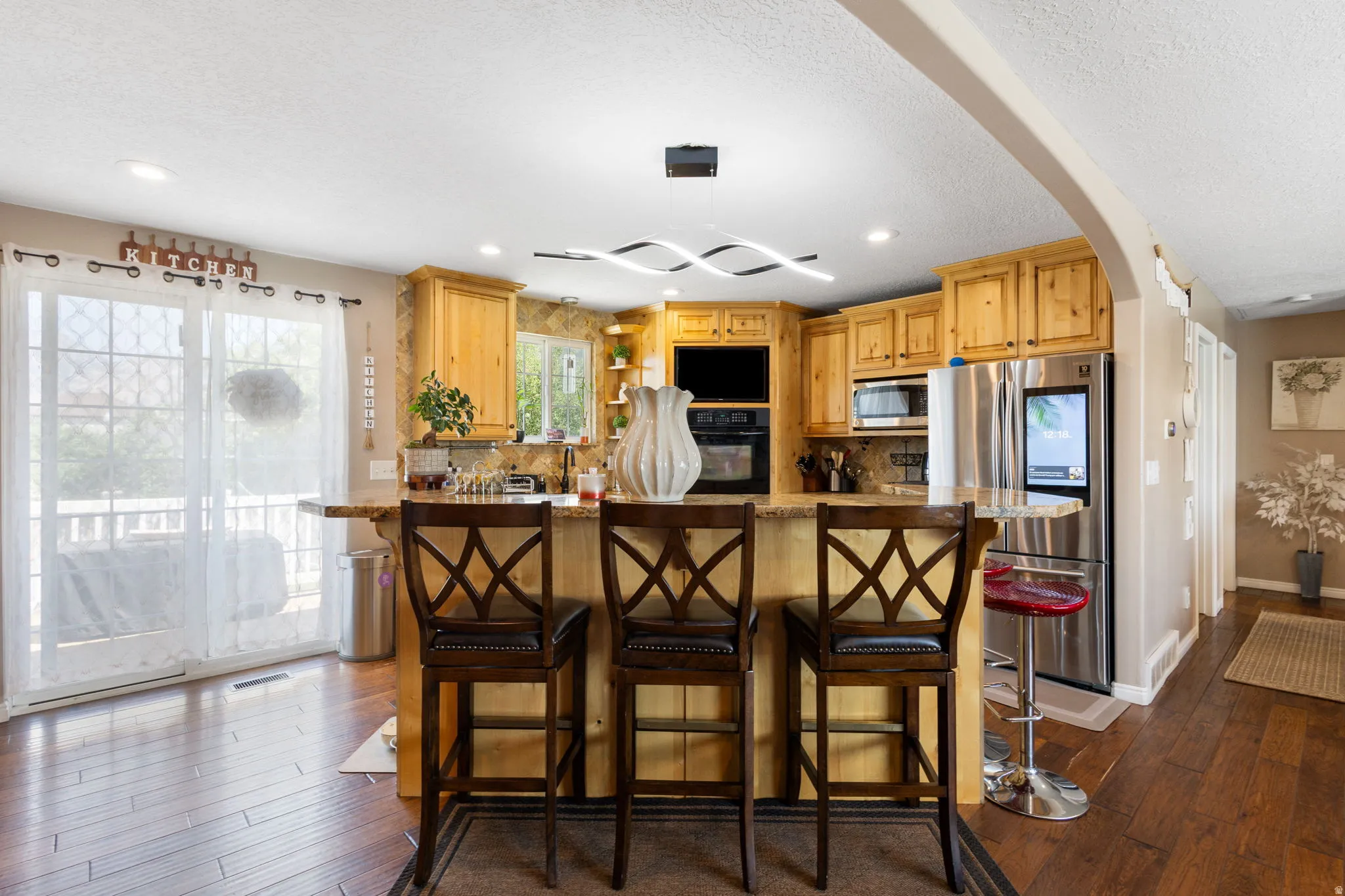 Kitchen featuring wood-finish flooring, light wood cabinetry, stone-finish countertops, stainless steel appliances, and a central island with seating