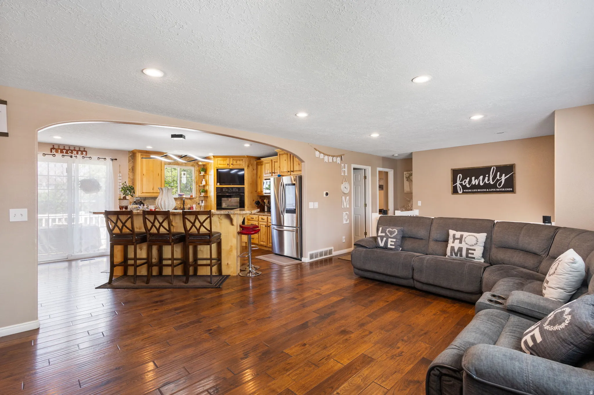 Wood-finish flooring throughout, recessed lighting, arched doorway, kitchen island with seating, and stainless steel appliances
