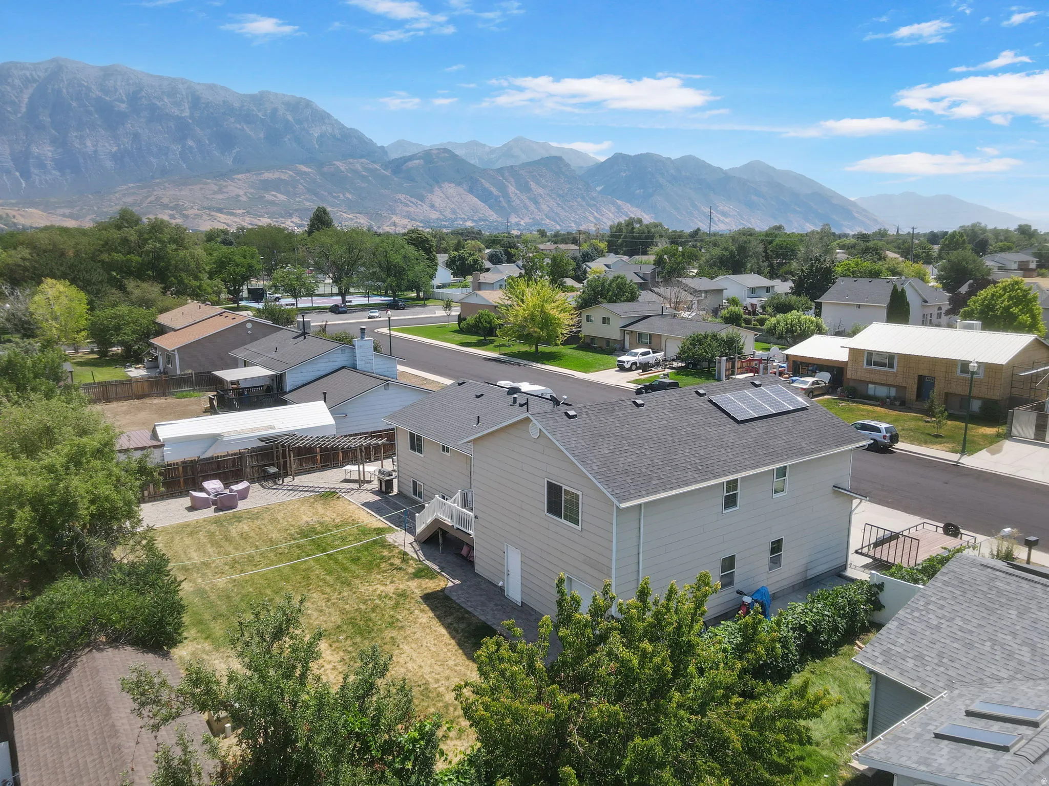 Mountain backdrop, solar panels, two-story exterior, shingled roof, paved patio