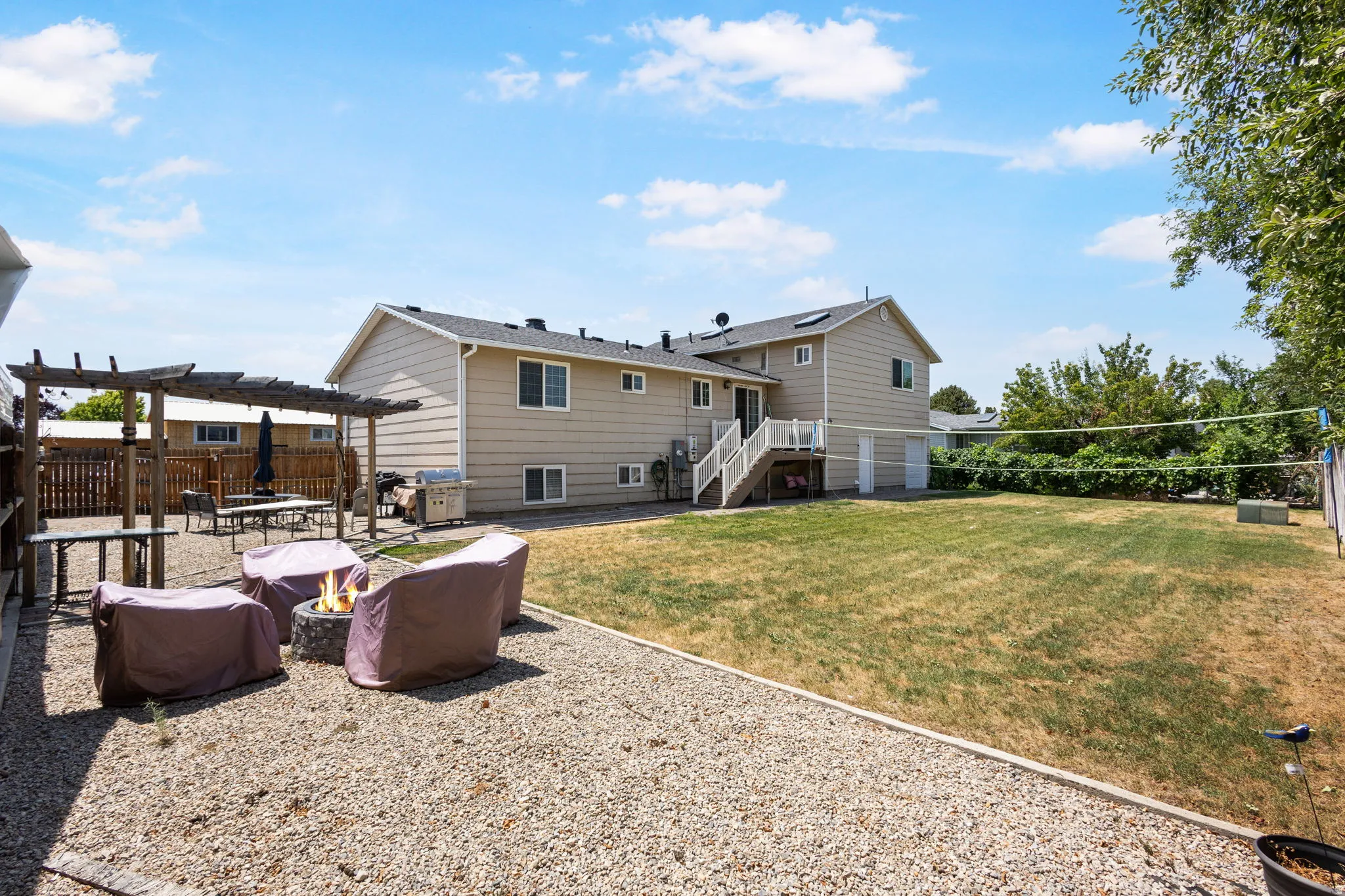 Expansive backyard featuring a gravel patio, pergola, fire pit, and a large lawn area