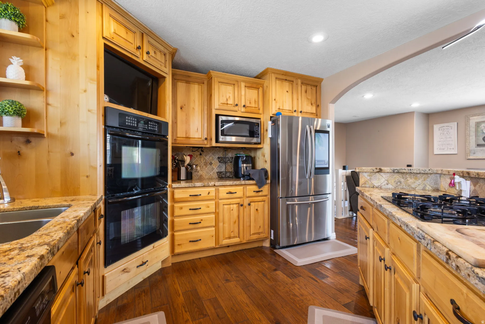 Wood-finish flooring, light wood cabinetry, stone countertops, stainless steel appliances, and a built-in double oven