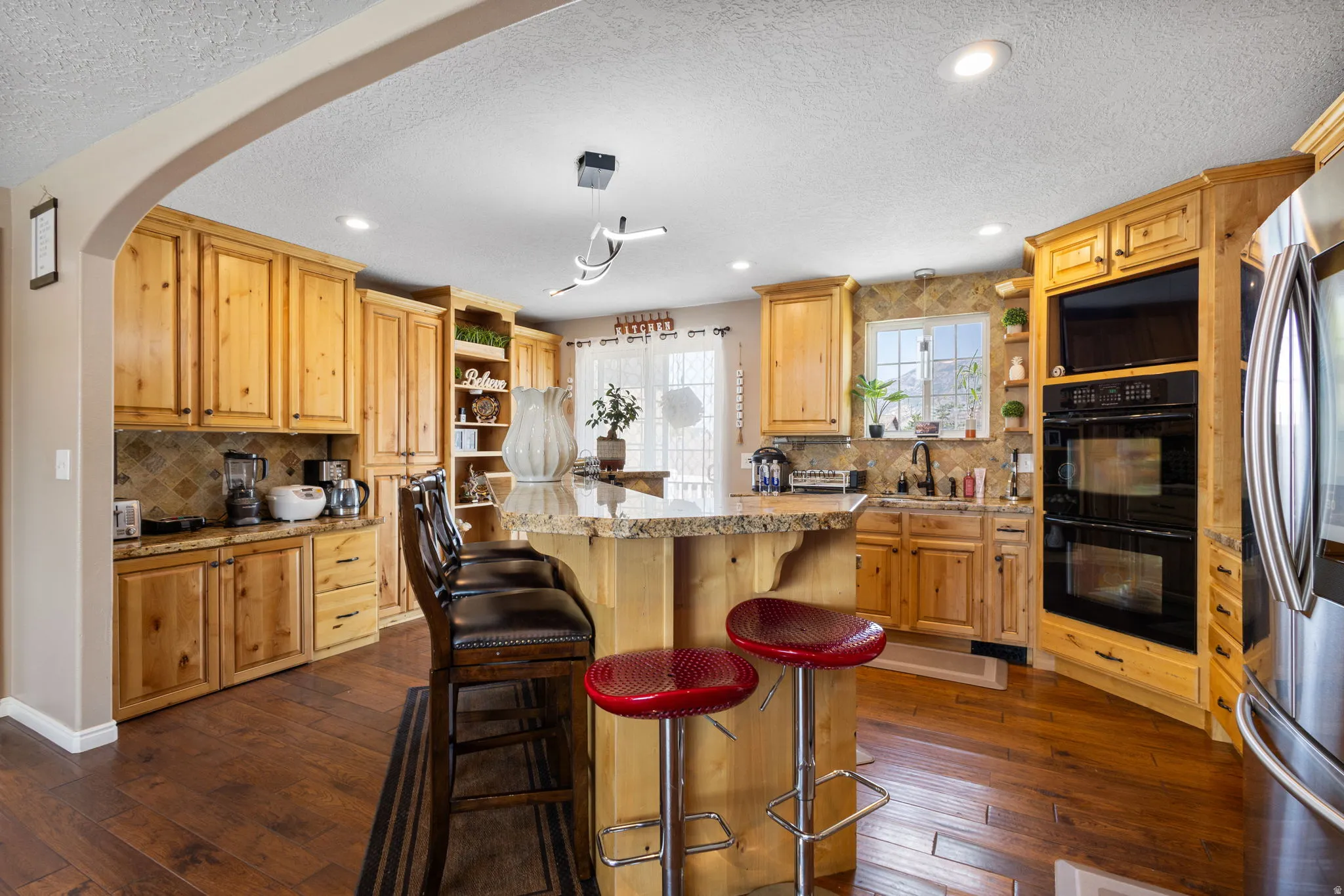 Gourmet kitchen featuring custom wood cabinetry, double wall ovens, a center island with bar seating, wood-finish flooring, and recessed lighting