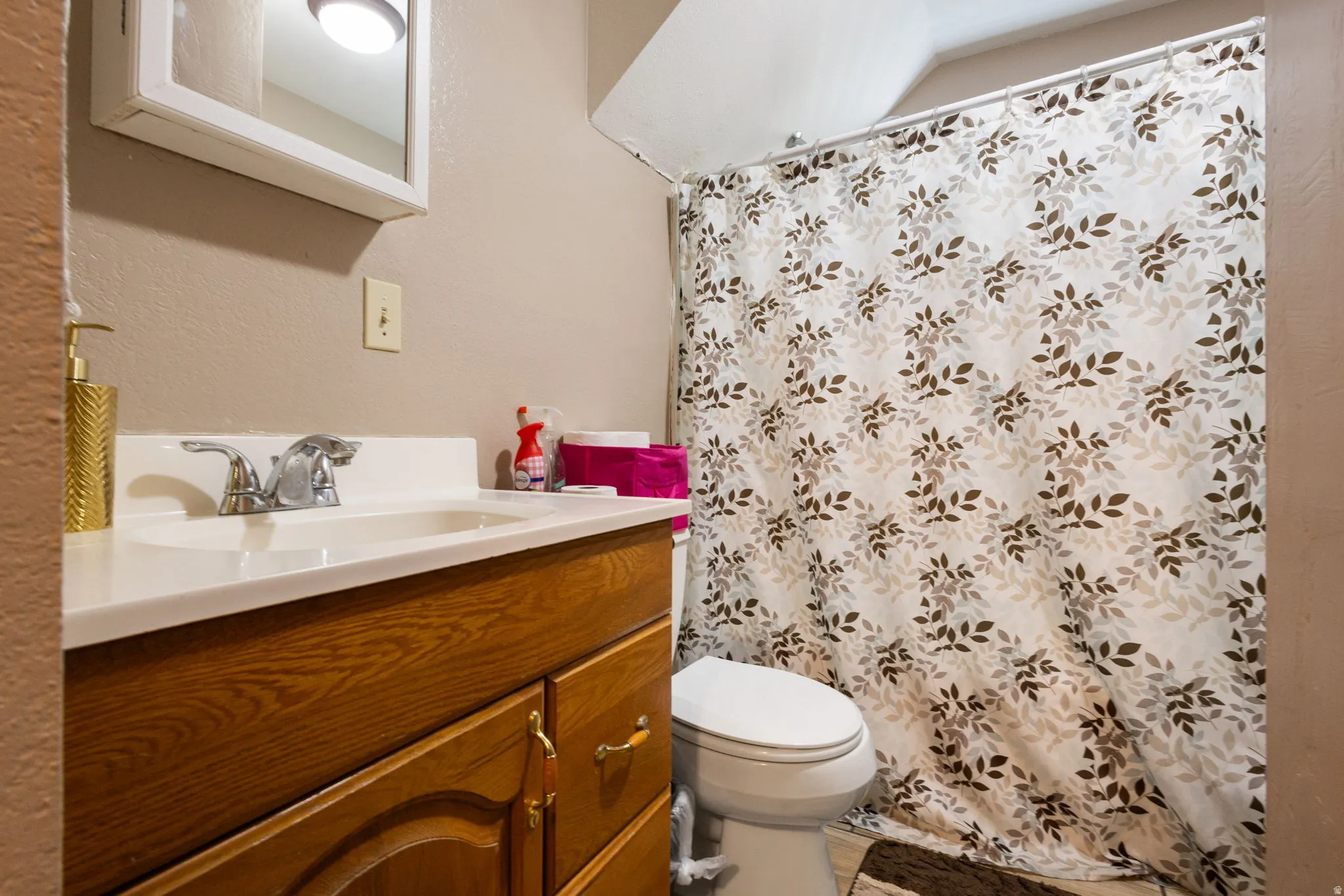 Bathroom featuring a wood-finish vanity with a white countertop and an integrated sink, polished chrome faucet, and a wall-mounted medicine cabinet with integrated lighting