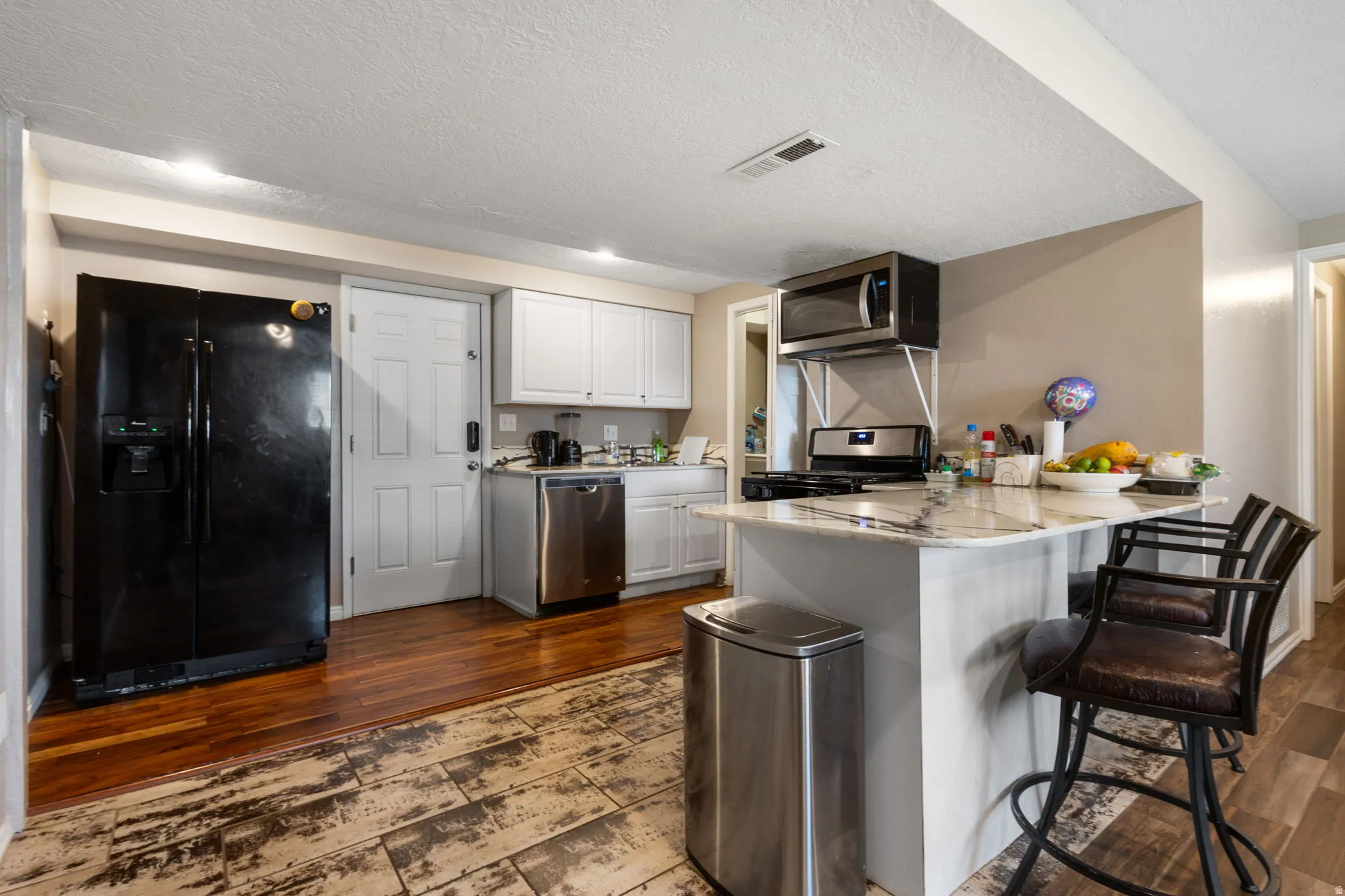 Kitchen featuring white cabinetry, stainless steel appliances, a center island with seating, and mixed wood-finish flooring