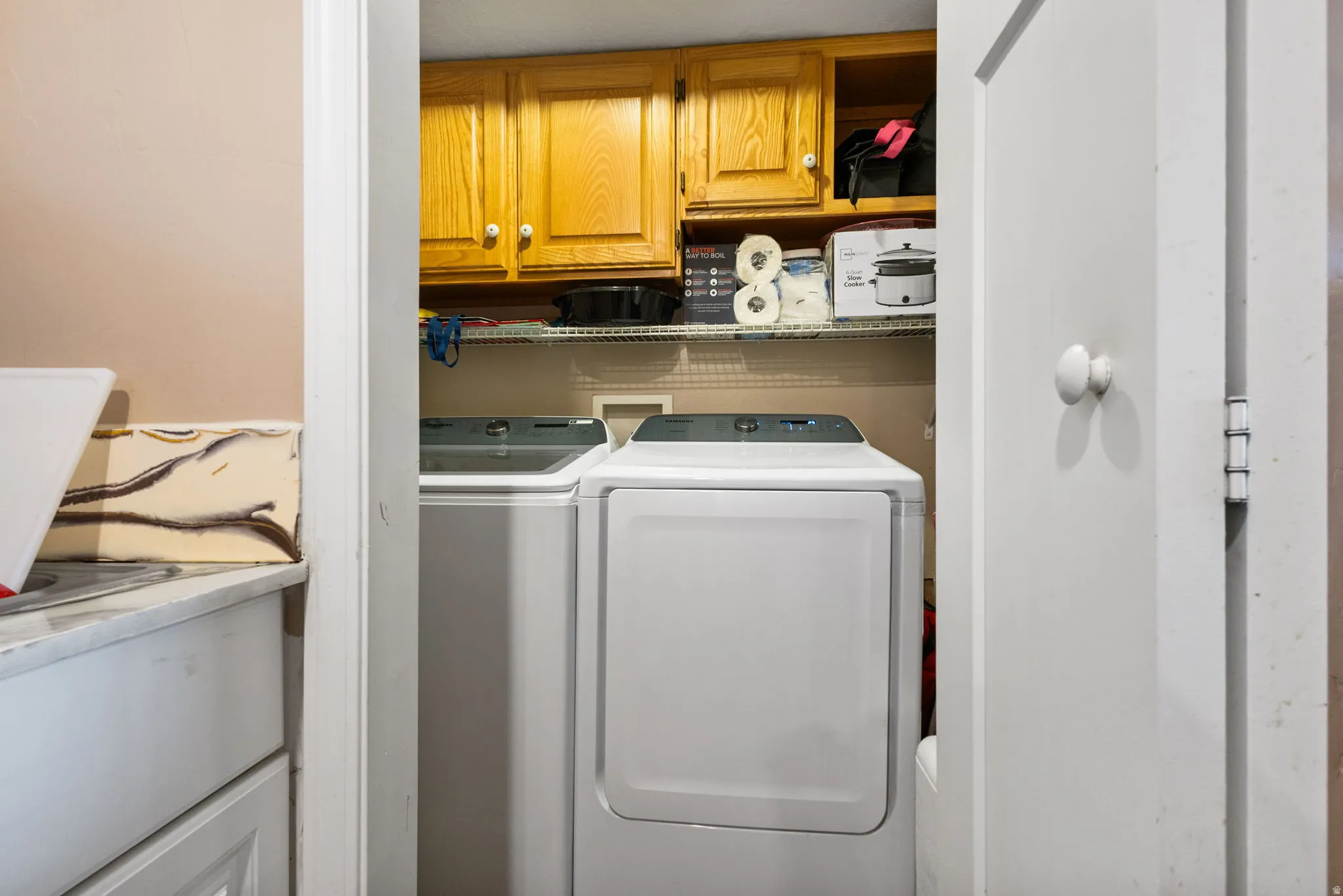 Dedicated laundry area featuring upper wood-finish cabinetry, wire shelving, and space for side-by-side appliances
