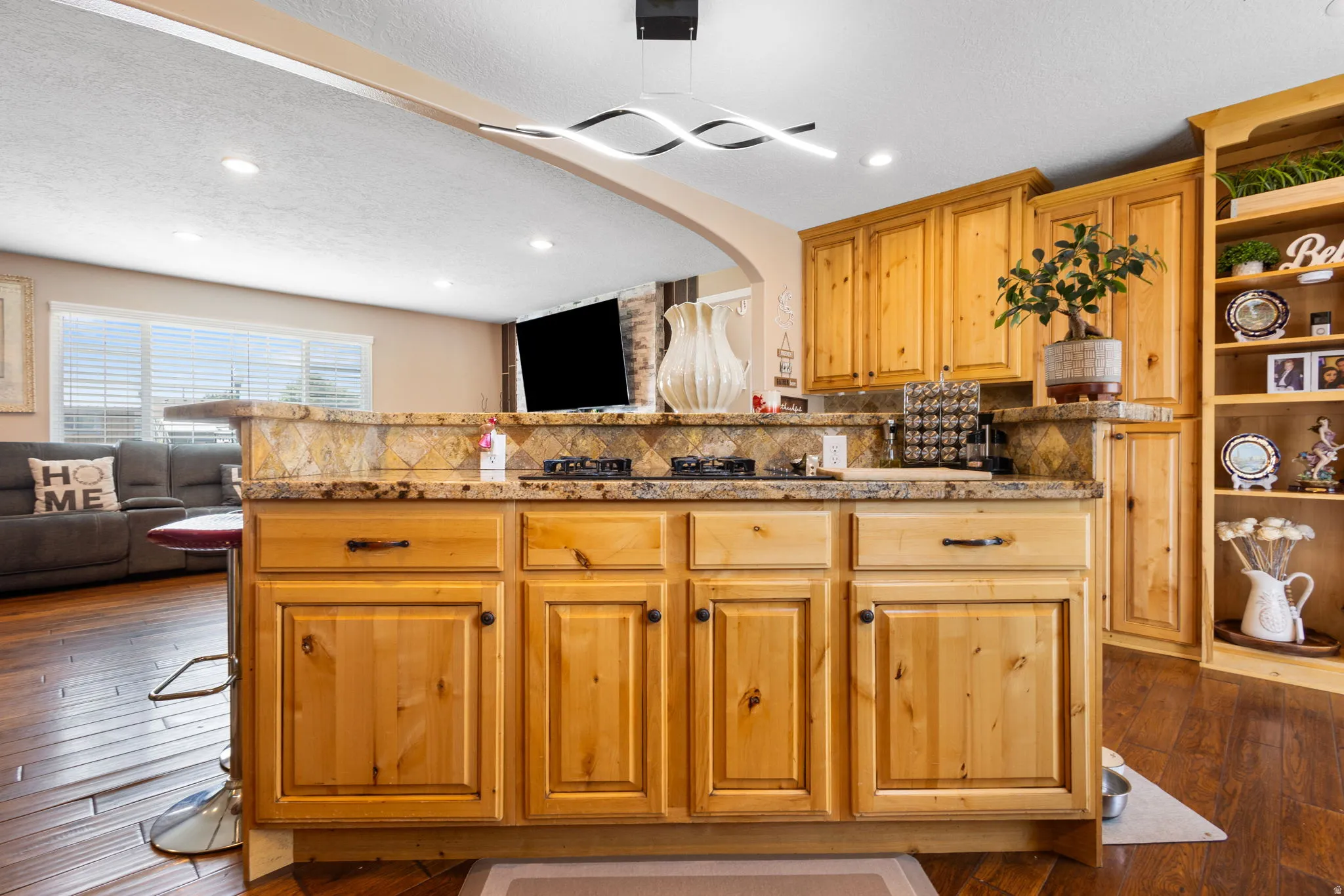 Kitchen island featuring wood cabinetry, integrated cooktop, and stone countertop