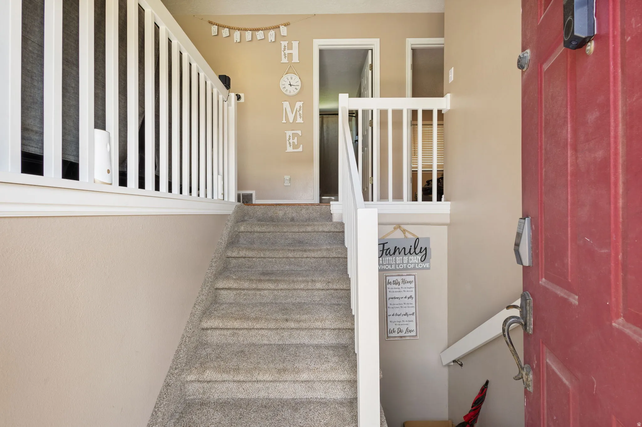 Entryway featuring a red paneled door, digital lock hardware, white balusters, and carpeted stairs