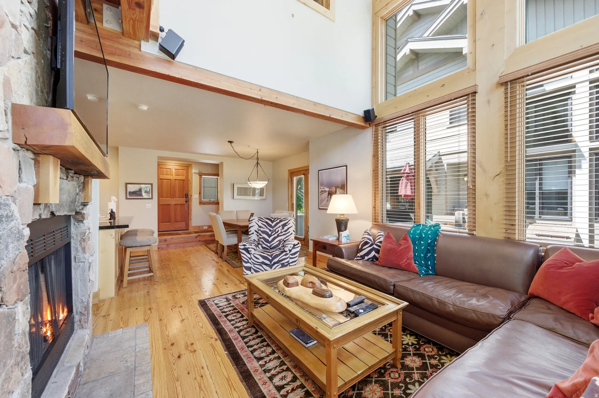 Stone-clad fireplace with wood mantle, high ceilings with exposed beams, wood-finish flooring, and expansive windows
