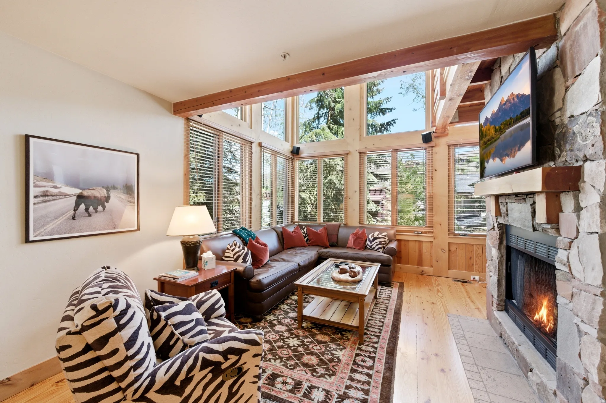 Stone-clad fireplace, wood-finish flooring, exposed wooden beams, and expansive windows