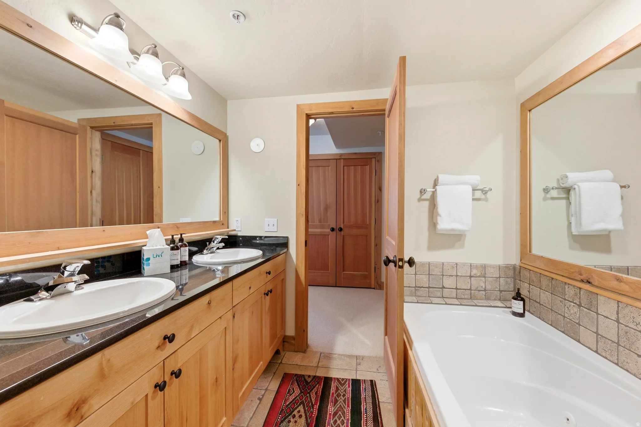 Spa-inspired primary bathroom featuring dual vanities with wood cabinetry, black countertops, and polished nickel fixtures