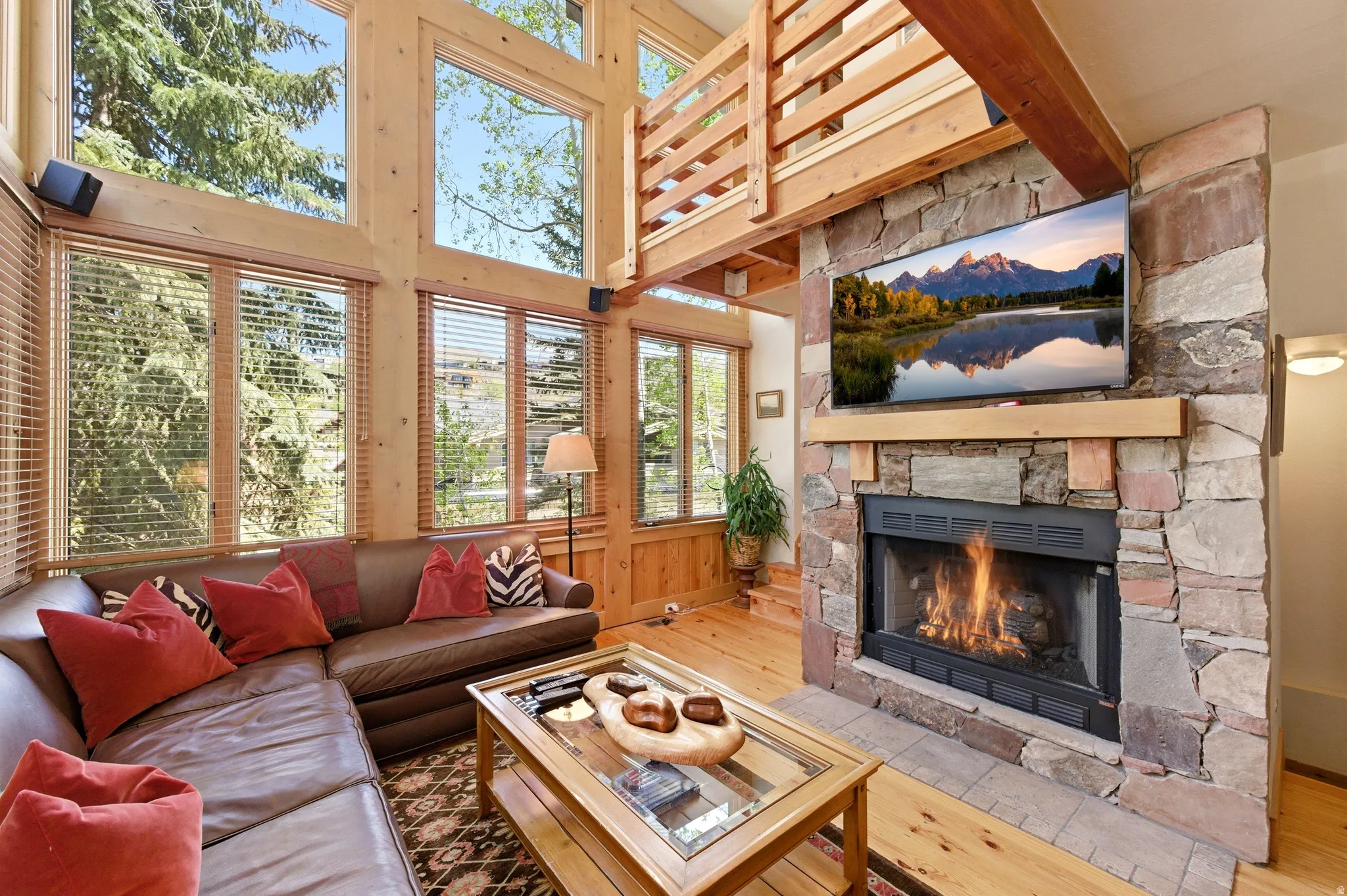 Vaulted ceiling with exposed wood beams, extensive natural wood window frames, stone-clad fireplace, built-in fireplace, and wood-finish flooring