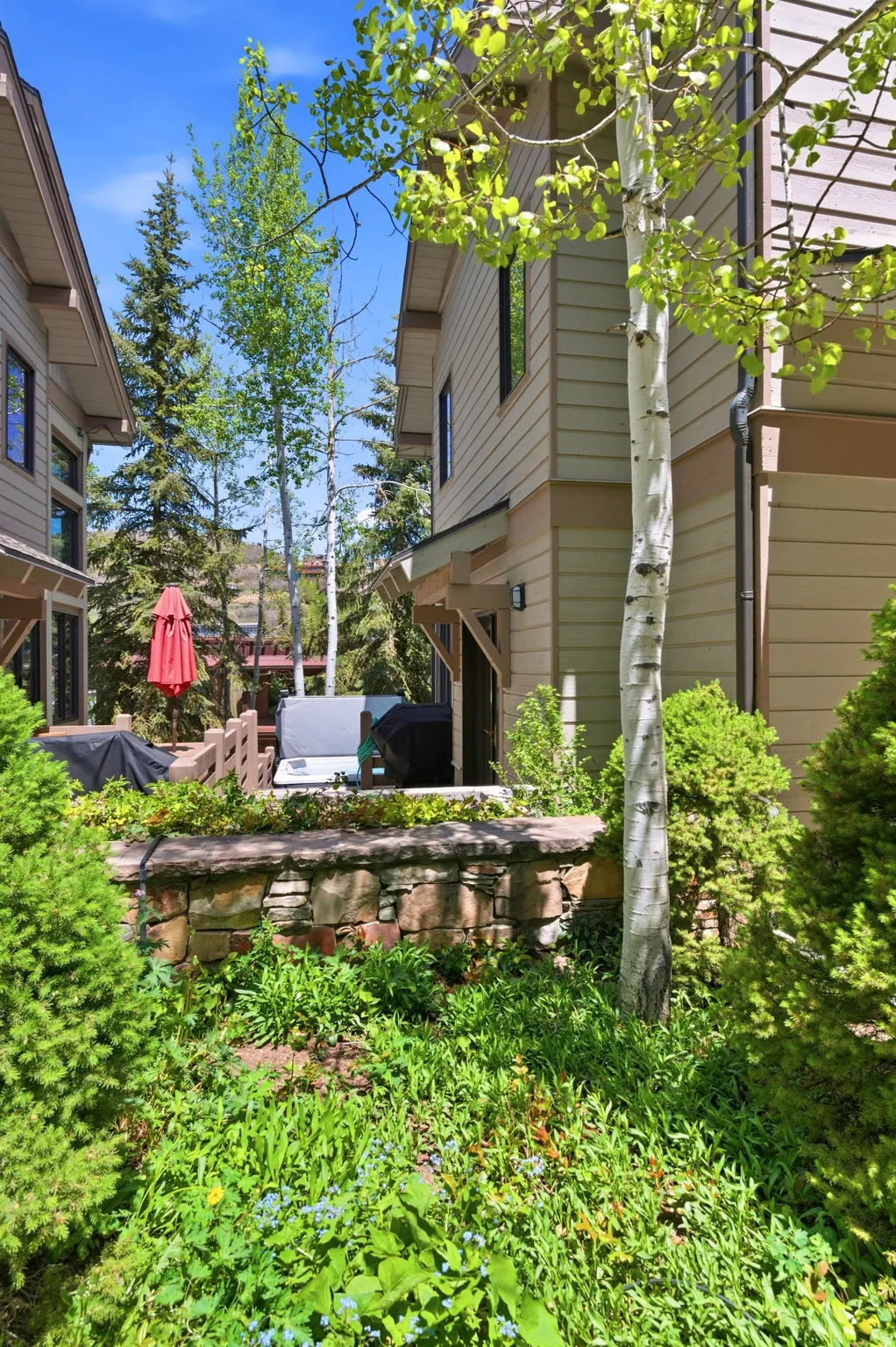 Exterior featuring horizontal siding, dark-trimmed windows, a stone retaining wall, and established landscaping