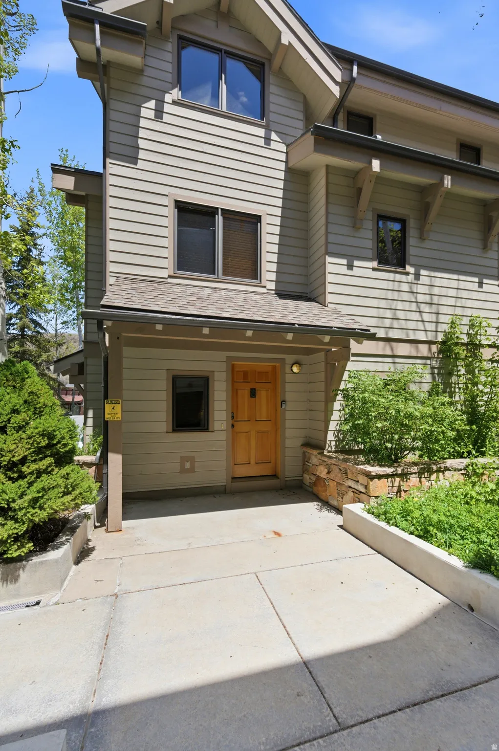 Modern multi-level residence featuring clean horizontal siding, a welcoming wood-finish entry door with sidelights, and a covered front entry
