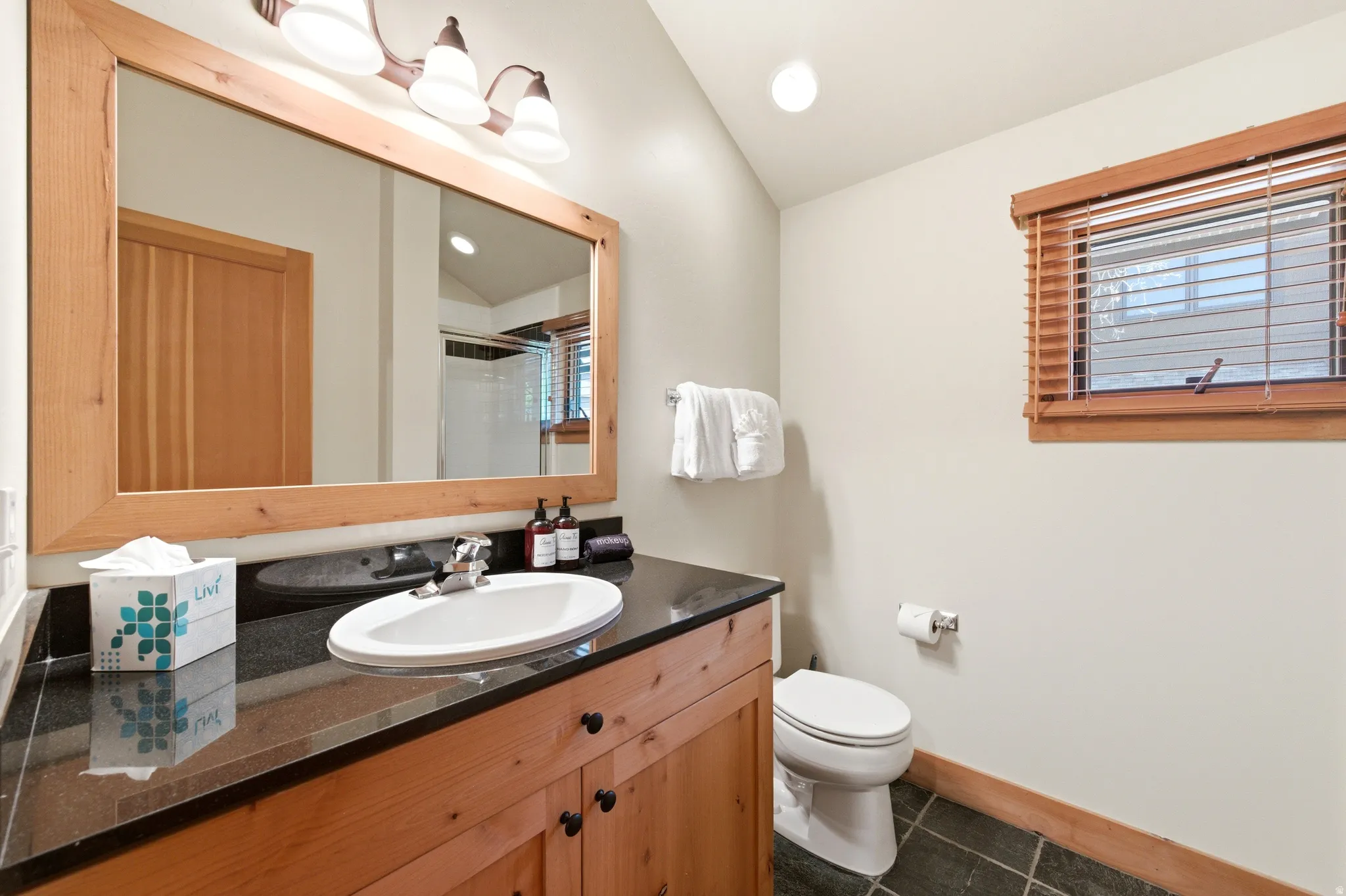 Wood-finish vanity with a dark countertop, undermount sink, and mounted mirror