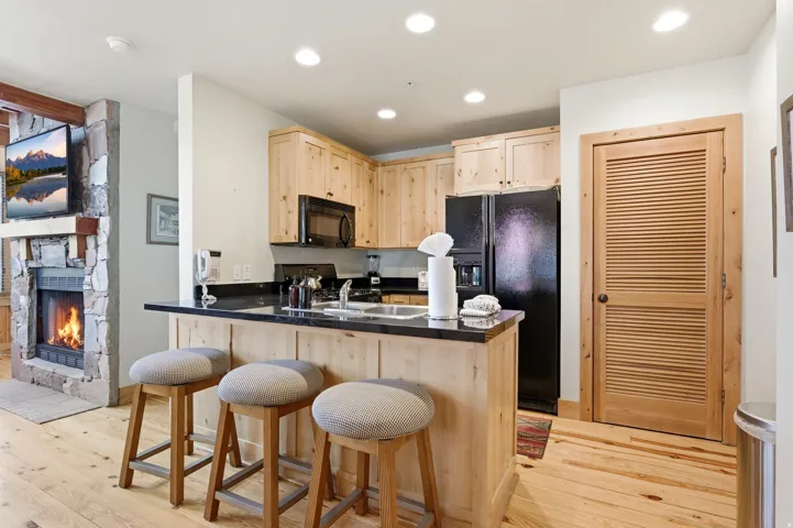 Contemporary kitchen featuring natural wood cabinetry, black quartz countertops, and stainless steel appliances