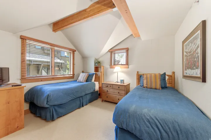 Bright, vaulted bedroom with exposed wood beam ceiling and multiple windows flooding the space with natural light