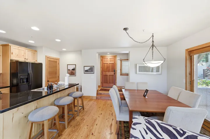 Open-concept kitchen and dining area featuring wood-finish flooring throughout, custom wood cabinetry with black stainless steel appliances, a multi-seat island with wood-frame seating, and a spacious dining table anchored by a pendant light fixture