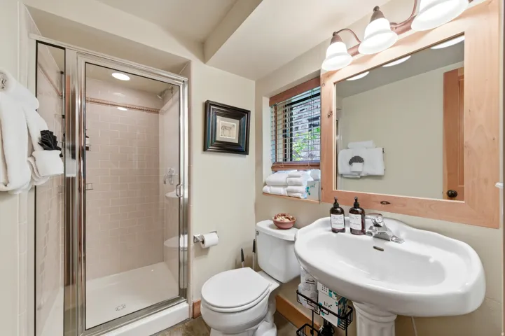 Pedestal sink, wood-finish mirror frame, walk-in shower with tile surround, window with blinds