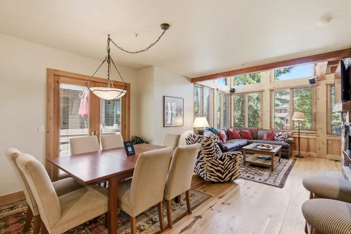 Open-concept living space featuring wood-finish flooring, exposed wood beams, and a wall of windows