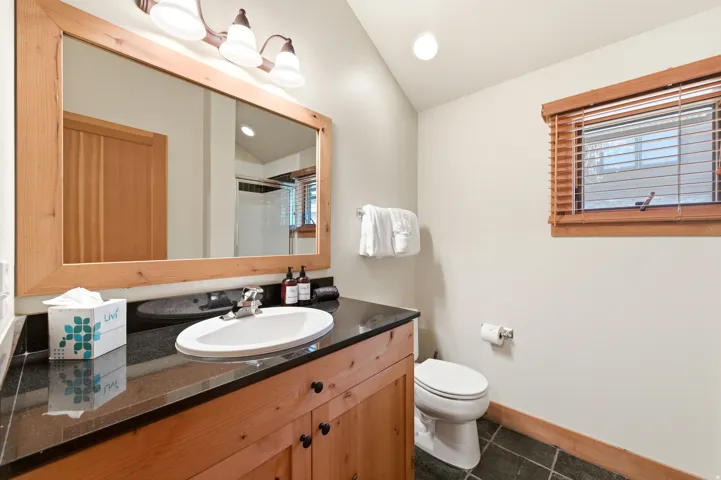 Wood-finish vanity with a dark countertop, undermount sink, and mounted mirror